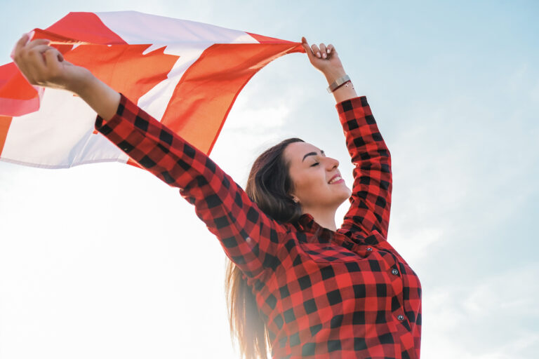 Happy newcomer holding Canadian flag outdoors