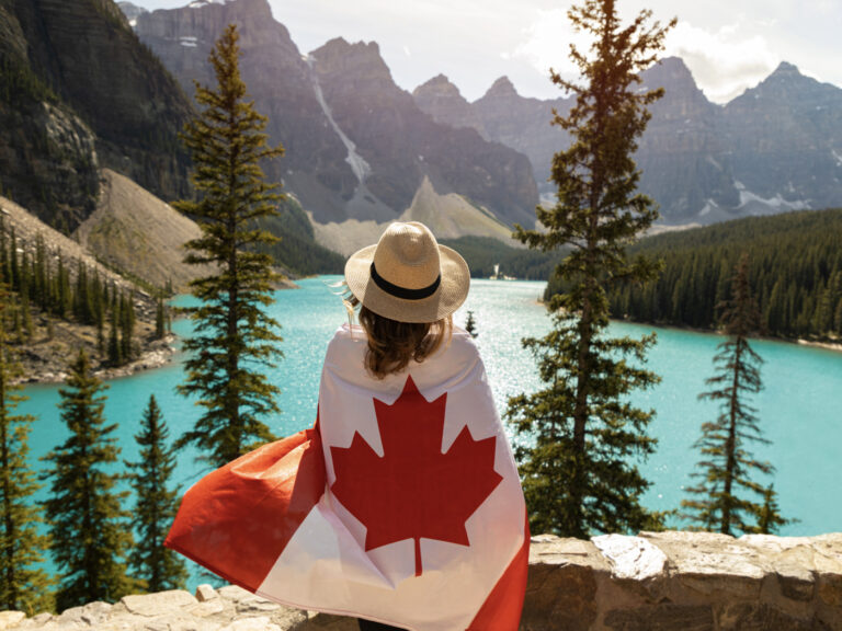 Newcomer in Canada wrapped in flag overlooking Moraine Lake